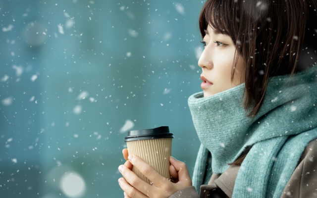 雪の舞う中、暖を取る女性